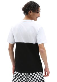 Zwart-witte T-shirt met korte mouwen en een horizontaal kleurblokontwerp; de achterkant toont de witte bovenhelft en de zwarte onderhelft.