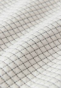 Tissu blanc avec un motif matelassé en diamants en relief subtil et de fines coutures noires le long des bords.