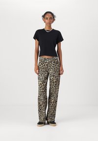 Crni skraćeni majica s kratkim rukavima, u kombinaciji s hlačama širokih nogavica s leopard uzorkom u smeškastoj i crnoj boji, i crnim cipelama sa smeškastom potplatom.