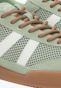 Zielona zamszowa sneakersy z białymi siateczkowymi wstawkami i brązowymi sznurówkami. Gumowa podeszwa jest jasnobrązowa, podkreślając sportowy design buta.