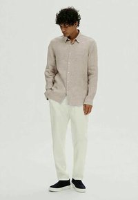 Lys beige lin skjorte med knappestilling foran, brukt med hvite bukser og marineblå slip-on joggesko. Antrekket har en avslappet passform.