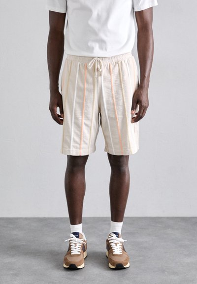 Shorts en maille beige pour homme avec des rayures verticales orange et jaune, taille élastique avec cordon de serrage, associés à des baskets marron et des chaussettes blanches.