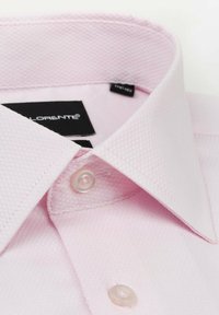 Jasnoróżowa koszula z tkaniny o fakturze, z ostrym kołnierzykiem i przezroczystymi guzikami. Wewnątrz kołnierzyka widoczna metka z nazwą marki.