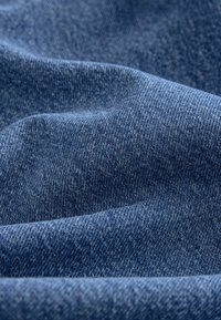 Mørkeblå denimstof med en tekstureret vævning, der har synlige stikningsmønstre og lette farvevariationer på overfladen.