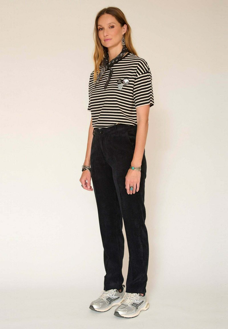 Chemise à rayures noir et blanc à manches courtes, pantalon en velours côtelé noir et baskets argentées ; inclut une écharpe noire et des accents de bijoux.