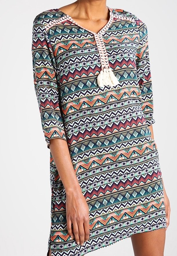 Monivärinen kangas, jossa on geometrisiä kuvioita, suunniteltu mekko. V-pääntie, jossa on virkattu nauha ja tupsut. Kolmannes erityksistä ja rento istuvuus.