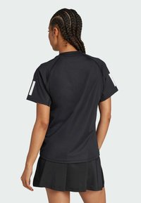 Cămășuță sport neagră cu mâneci scurte și design raglan, asortată cu o fustă plisată neagră. Material neted cu accente albe pe mânecă.