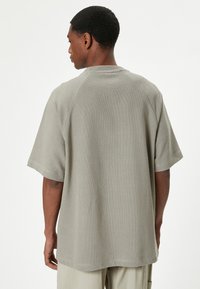 Grå kortærmet t-shirt med en struktureret strikfinish og raglanærmer, der har en rund halsudskæring og en afslappet pasform.