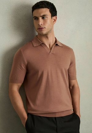 Tricou polo cu mânecă scurtă, de culoare maro deschis, cu guler în V și material texturat, asortat cu pantaloni negri. Design moale, ajustat, fără modele vizibile.