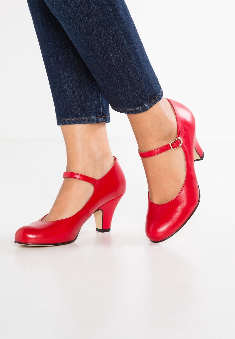 Escarpins en cuir rouge avec un bout arrondi, une bride à la cheville et un talon de hauteur modérée. Texture lisse et finition brillante. Portés avec un denim foncé.