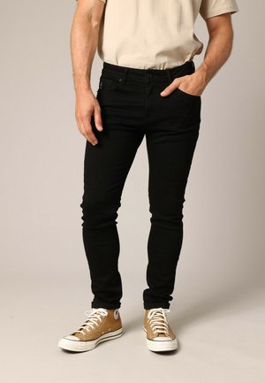 Zwarte denim jeans met een slim fit, vijf zakken en zichtbare stiksels, gecombineerd met tan hoge sneakers.