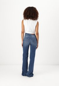 Λευκό κομμένο τοπ χωρίς μανίκια με κατσαρό στρίφωμα, σε συνδυασμό με φαρδιά μπλε τζιν πουκάμισα με δύο πίσω τσέπες και ξεθωριασμένη υφή.