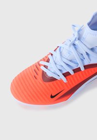 Kaugelähedalt vaadatud ereoranž ja valge Nike spordijalanõud helesiniste paeltega valgel taustal.