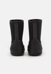 Botas de tobillo impermeables negras con una base de goma suave, suela de agarre texturizada y caña de tela suave con un detalle de costura vertical.