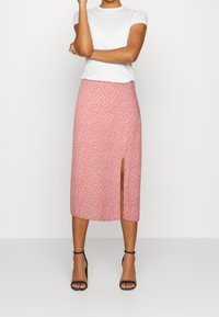 Vaaleanpunainen kukkakuosisempi midi-hame, jossa on sivureikä, valmistettu pehmeästä kankaasta. Yhdistetty tiukkaan valkoiseen t-paitaan ja mustiin korkokenkiin.