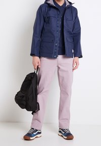 Navy waterproof jacket with a hood, four front pockets; paired with light pink pants and blue sneakers with white and brown accents.
