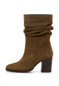 Botín de ante marrón hasta el tobillo con un diseño flojo, puntera cuadrada y tacón apilado. Presenta un sutil detalle del logo en el lateral.