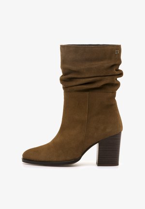 Botín de ante marrón hasta el tobillo con un diseño flojo, puntera cuadrada y tacón apilado. Presenta un sutil detalle del logo en el lateral.