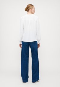 Weiße strukturierte Bluse mit Puffärmeln und elastischen Manschetten, kombiniert mit weit geschnittenen blauen Jeans. Einfaches Design, minimalistische Details.