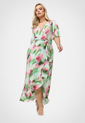 Kvinde går i en flydende slå-om-kjole med et abstrakt blomsterprint i grøn, pink og hvid, kombineret med nøgenfarvede højhælede sandaler.