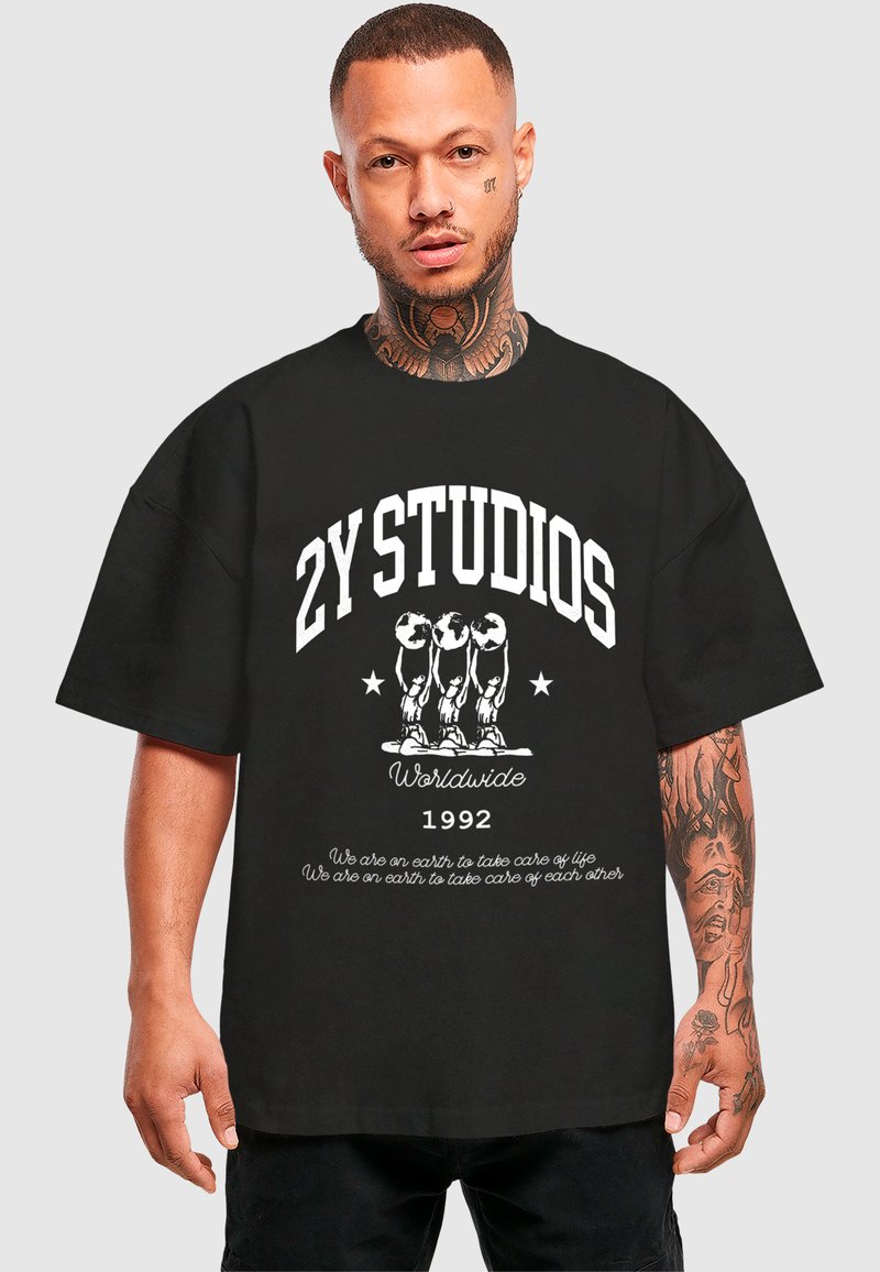 Fekete, oversized T-shirt fehér szöveggel és grafikával. Tartalmazza a "2Y STUDIOS" és a "Worldwide 1992" feliratokat, valamint három figurát, amelyek hangsúlyozzák az elülsőt.