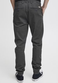 Mørk grå joggebukser med elastiske mansjetter, med baklommer, kontraststing, og brukt med svart og hvit sneakers.