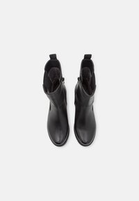 Botines de cuero negro hasta el tobillo con punteras redondeadas, paneles laterales elásticos y lengüetas, mostrados en vista superior sobre un fondo blanco.