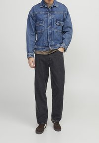 Blå denimjacka med två framsidor fickor, bärs över en grå skjorta. Mörkgrå jeans och bruna sneakers kompletterar outfiten.