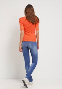 Orange ribbed top with lace cuffs paired with light blue skinny jeans. The jeans feature decorative stitching on the back pockets.