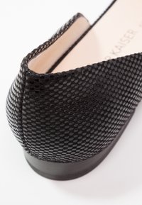 Chaussure noire avec une surface en maille texturée et un talon lisse. L'intérieur est de couleur claire, contrastant avec le design extérieur.