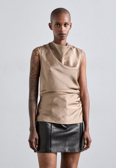 Haut sans manches en tissu beige au toucher lisse, associé à une minijupe ajustée en cuir noir.