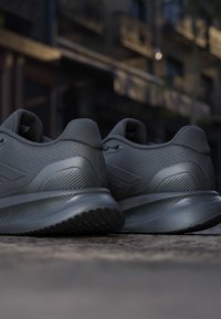 Pair of dark gray athletic running shoes placed side by side on a textured ground with blurred urban background.