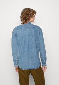 Camicia di jeans azzurro chiaro con maniche lunghe, polsini con bottoni, colletto a punta e cucitura a yoke sul retro. Texture morbida e vestibilità comoda.