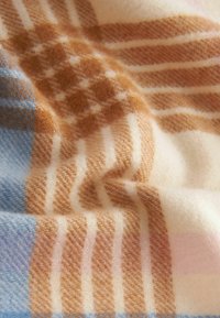 Wollwurfdecke mit kariertem Muster in Hellblau, Beige und Braun. Weiche Textur mit variierenden Streifenbreiten und -farben.