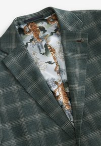 Blazer a quadri verdi con foderatura grigia in satin, caratterizzato da un motivo di tigri e fiori. Dettagli notevoli includono reverse strutturati e accessori metallici accentati.