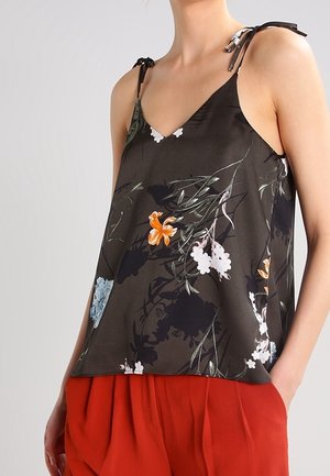 Top in tessuto leggero con stampa floreale scura, dotato di spalline regolabili, caratterizzato da fiori arancioni e bianchi su uno sfondo nero, abbinato a pantaloni rossi.