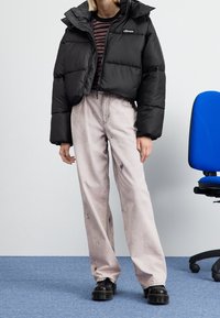 Czarna krótka kurtka puchowa z wysokim kołnierzem, zestawiona z jasnoróżowymi, luźnymi spodniami z przetarciami oraz czarnymi masywnymi butami.