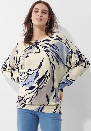 Strickpullover in Creme und Blau mit abstrakten Blumenmustern, Fledermausärmeln und rundem Ausschnitt. Kombiniert mit blauen Jeans.