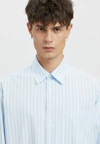 Lyseblå stripete skjorte med button-down krage, brystlomme og teksturert stoff. Har hvite og pastellstripede kontraster.