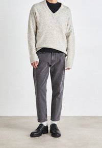 Pull en maille texturée gris clair avec un col en V ; T-shirt noir en dessous. Jean droit gris foncé et chaussures à lacets noires à semelles épaisses.