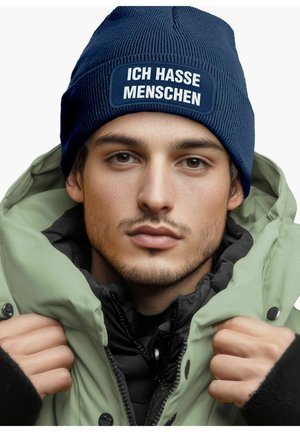Navy ribbed beanie with white text "ICH HASSE MENSCHEN" on a patch; model wears a green jacket with a black inner lining.