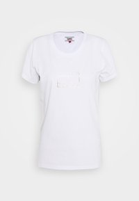 Bílý krátký rukáv T-shirt s výstřihem do V a malým kovovým logem "Tommy Jeans" umístěným na středu hrudi.