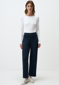 Witte lange mouwen ribbeltop gecombineerd met wijde, textuur donkerblauwe broek en witte sneakers. Eenvoudig, aansluitend ontwerp met zachte contouren.