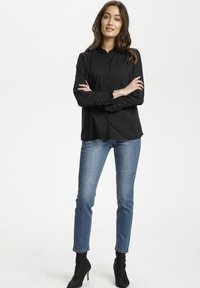 Melna garām piedurknēm krekls ar volānu apkakli un aprocēm, pogu priekšpuses dizains, apvienots ar ziliem šauriem džinsiem un melniem potīšu zābakiem.