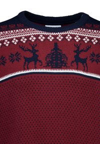Rot gestrickter Pullover mit einem Fair-Isle-Muster aus marineblauen Rentieren und Schneeflocken. Runde Ausschnitt mit weißem Akzentstreifen. Strukturierten Stoff.