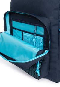 Interno di uno zaino navy con tasca con cerniera turchese, sezione in rete e pannelli organizzativi. Tessuto liscio e texture robusta.