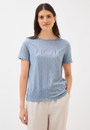 Camiseta de manga corta azul con un patrón de hojas y la palabra "ALOHA" en un color claro en la parte delantera. Hecha de una tela suave y ligera.