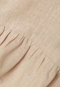 Tessuto di lino beige chiaro con una morbida texture presenta un dettaglio di volants arricciati lungo il bordo, creando un sottile effetto a strati.