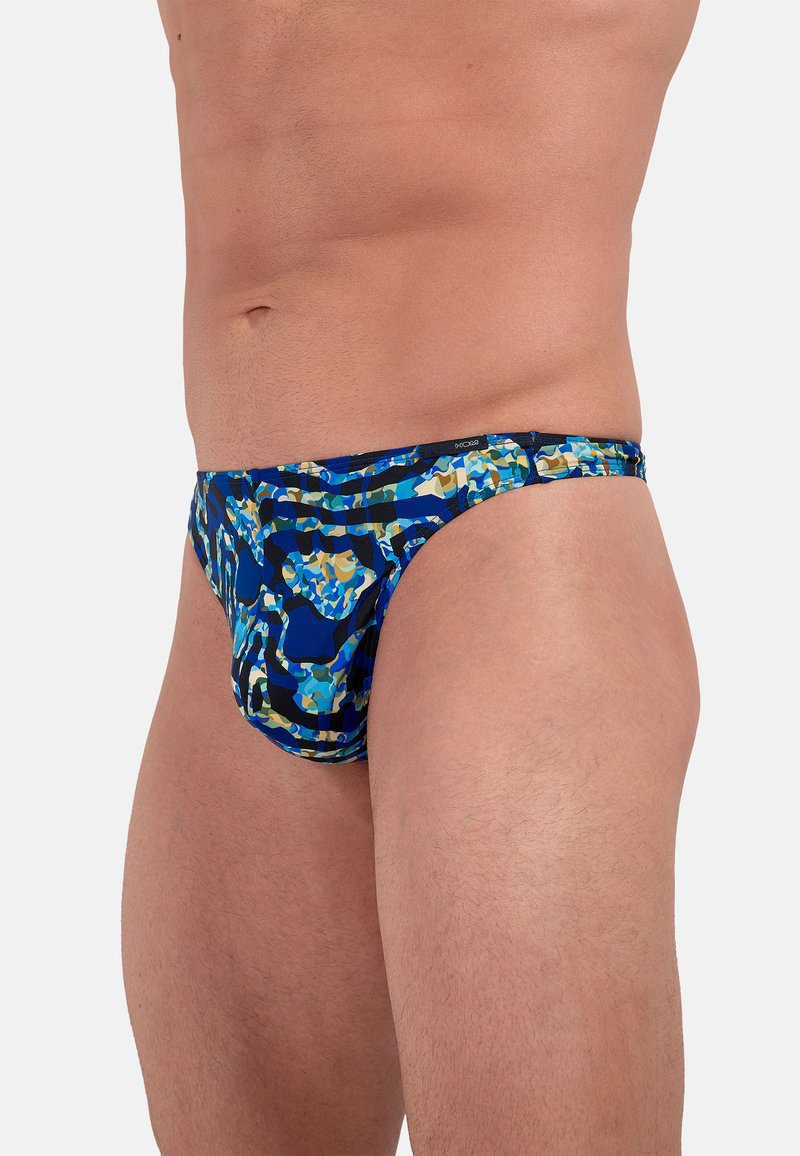 Blaue und camouflage-musterte Badebrieftails aus dehnbarem Material, mit einem tiefen Schnitt und einem kontrastierenden Bund für einen sicheren Sitz.