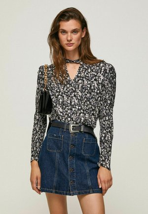 Blusa floreale bianca e nera con maniche lunghe e scollatura a V, abbinata a una gonna di jeans con bottoni frontali e una cintura nera.